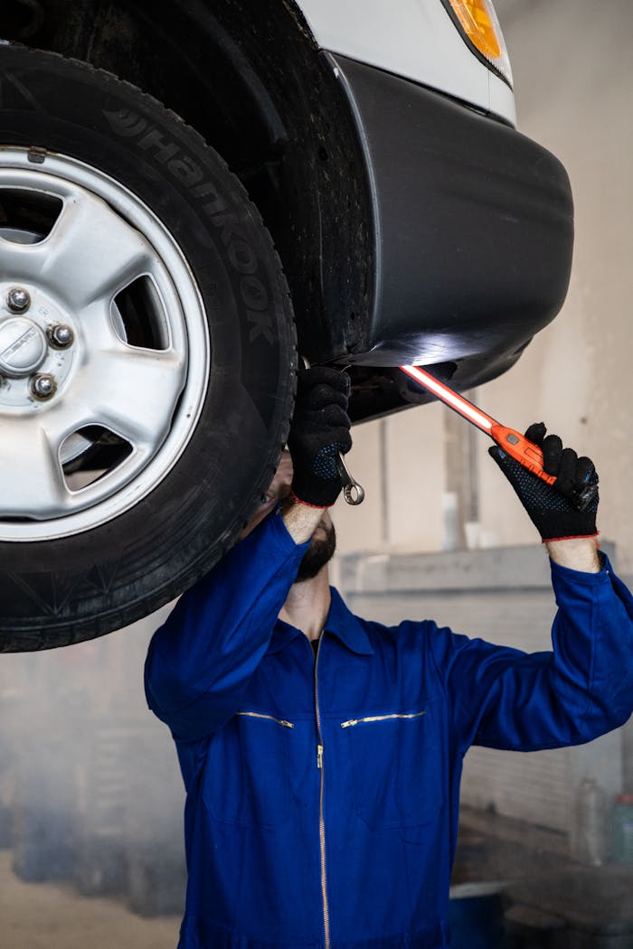 Mechanic inspecting a car in an auto repair shop, checking under the vehicle with a flashlight.