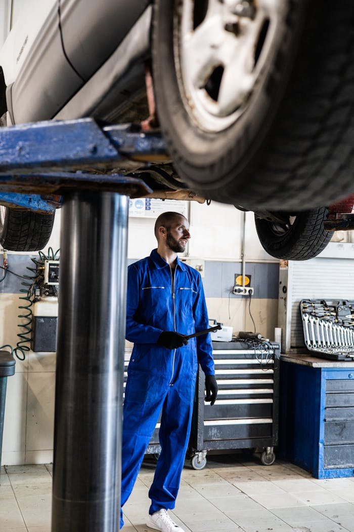 Mechanic in blue coverall inspecting vehicle in an auto repair shop. Professional car maintenance concept.